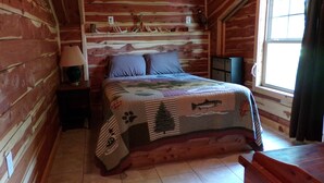 A wooden cabin bedroom with a bed, a nightstand, a lamp, and a window. - Cedar Cabin Located on a Buffalo Farm Near the Buffalo National River (Marshall)