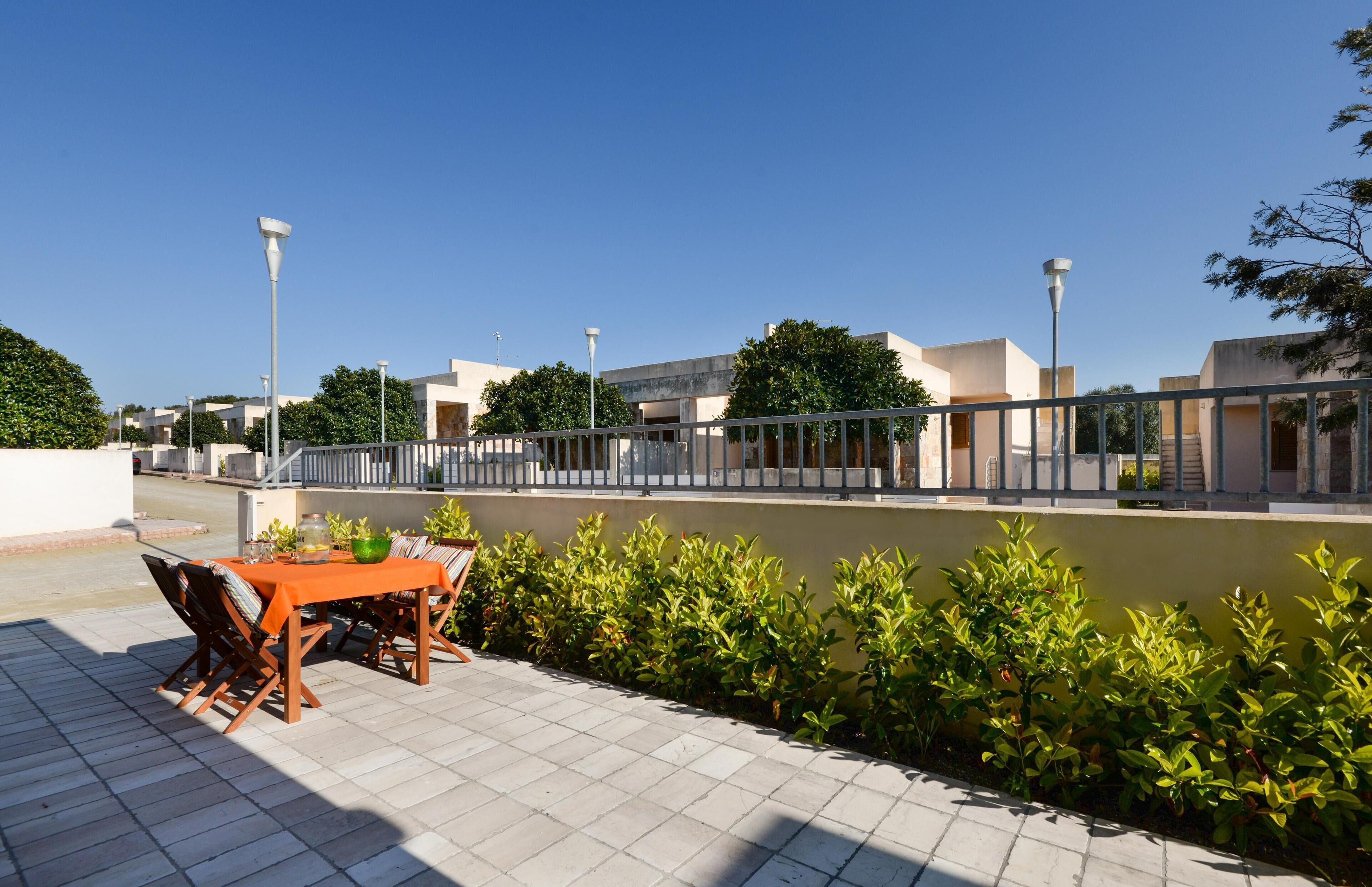 A patio area with a table and chairs, a railing, and a view of buildings across a water body.