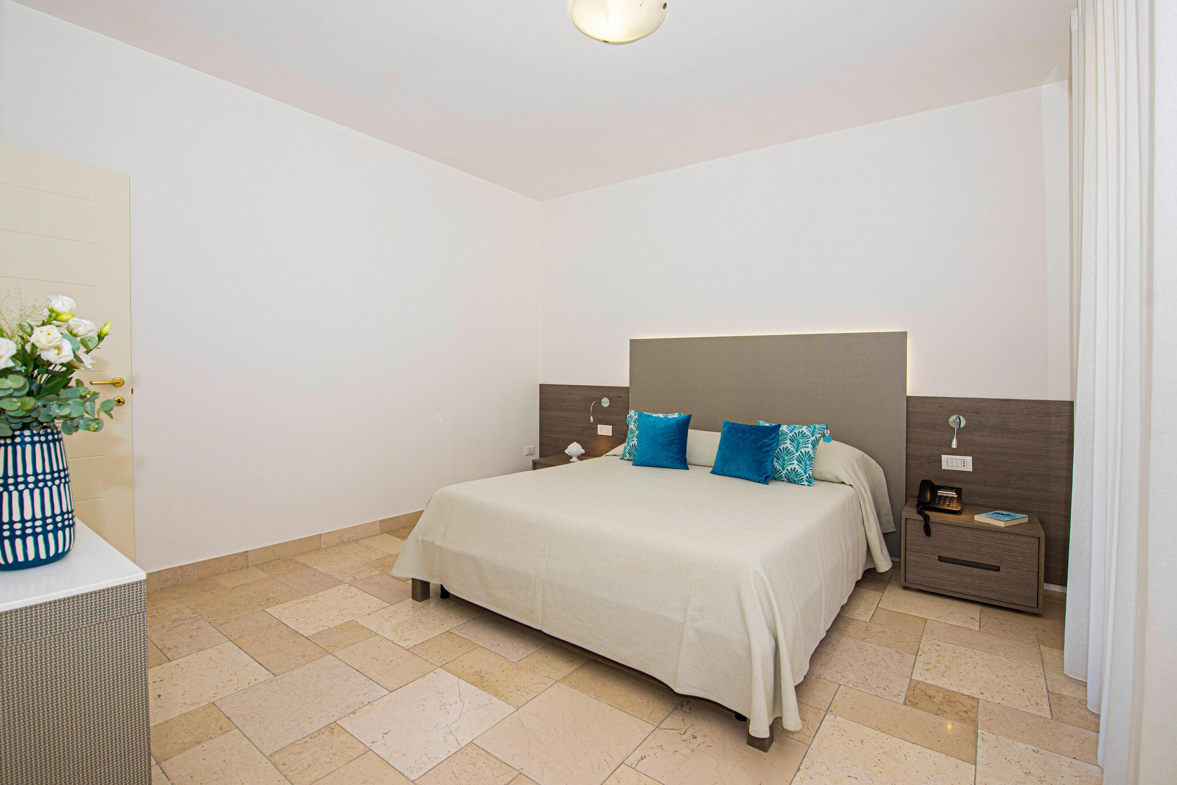 Un dormitorio ordenado con cama, mesitas de noche y velador.