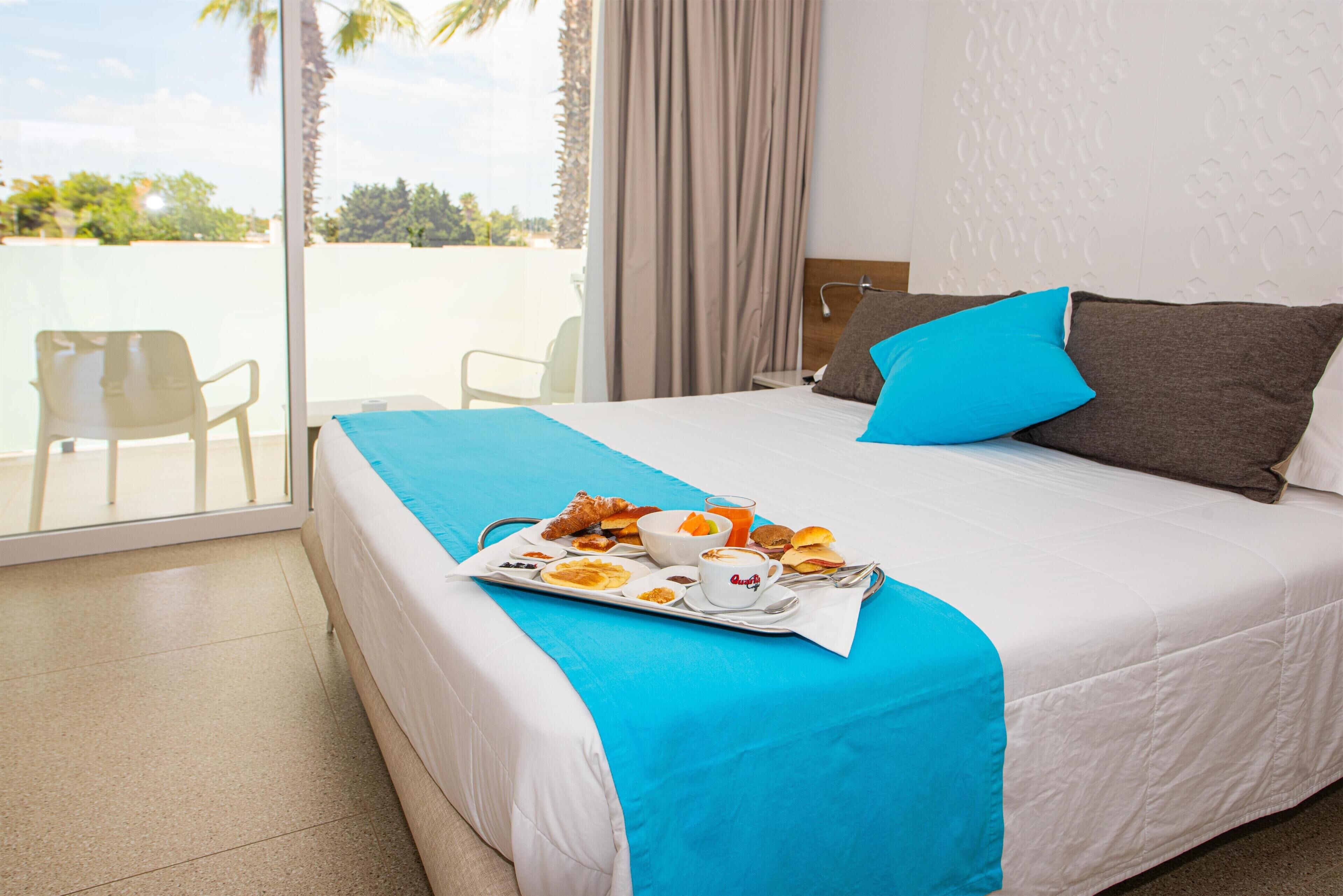 A hotel room with a bed, a breakfast tray, and a view of palm trees.