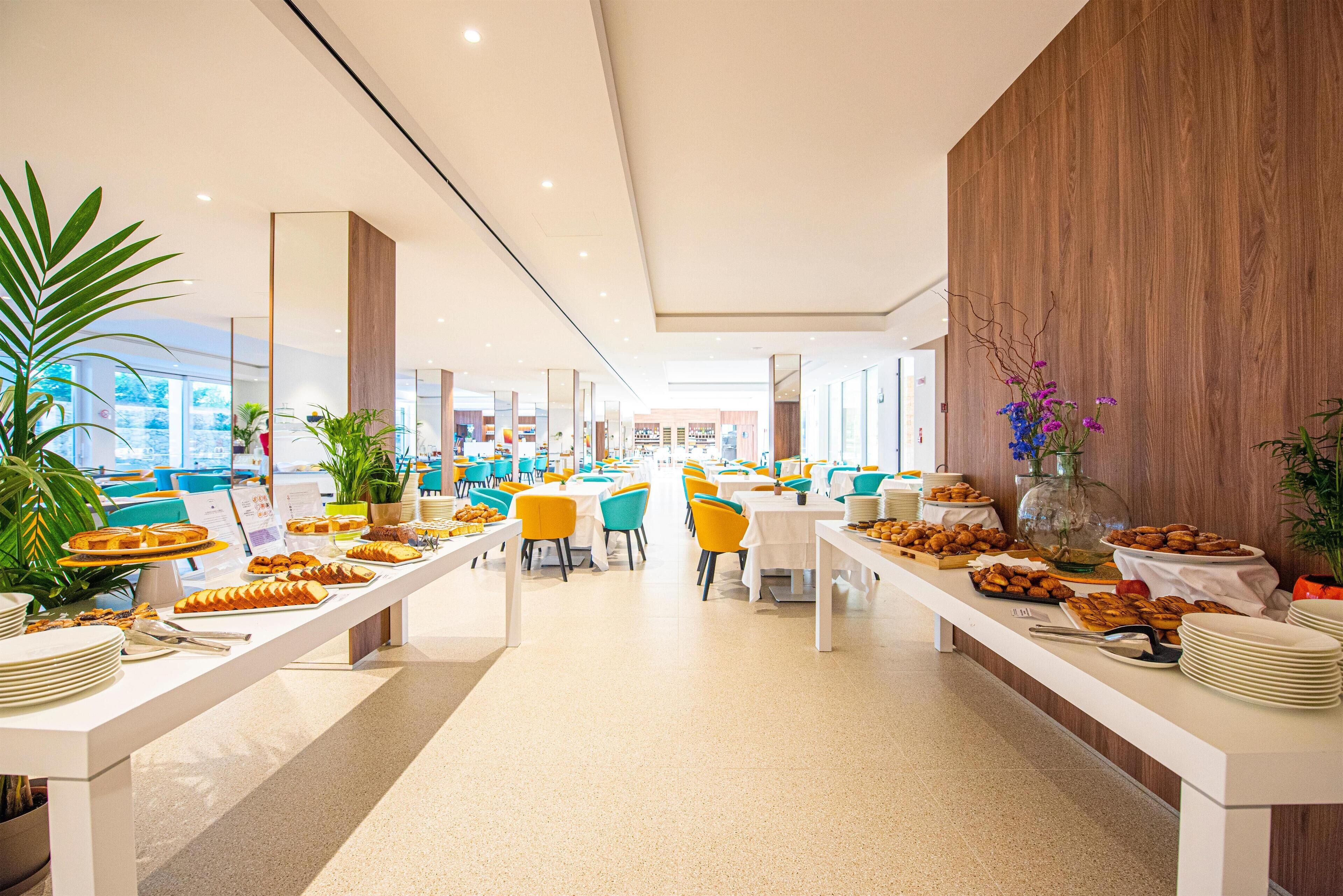 Un comedor moderno con mesas largas, sillas coloridas y diferentes opciones de comida.