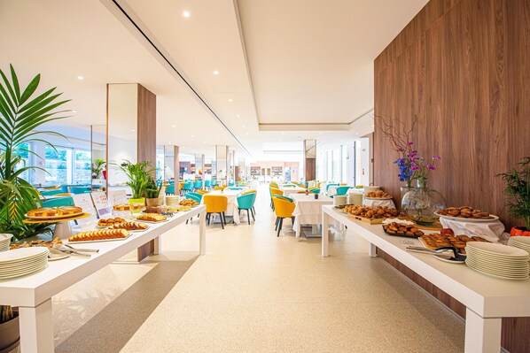 A modern dining area with long tables, colorful chairs, and various food items.