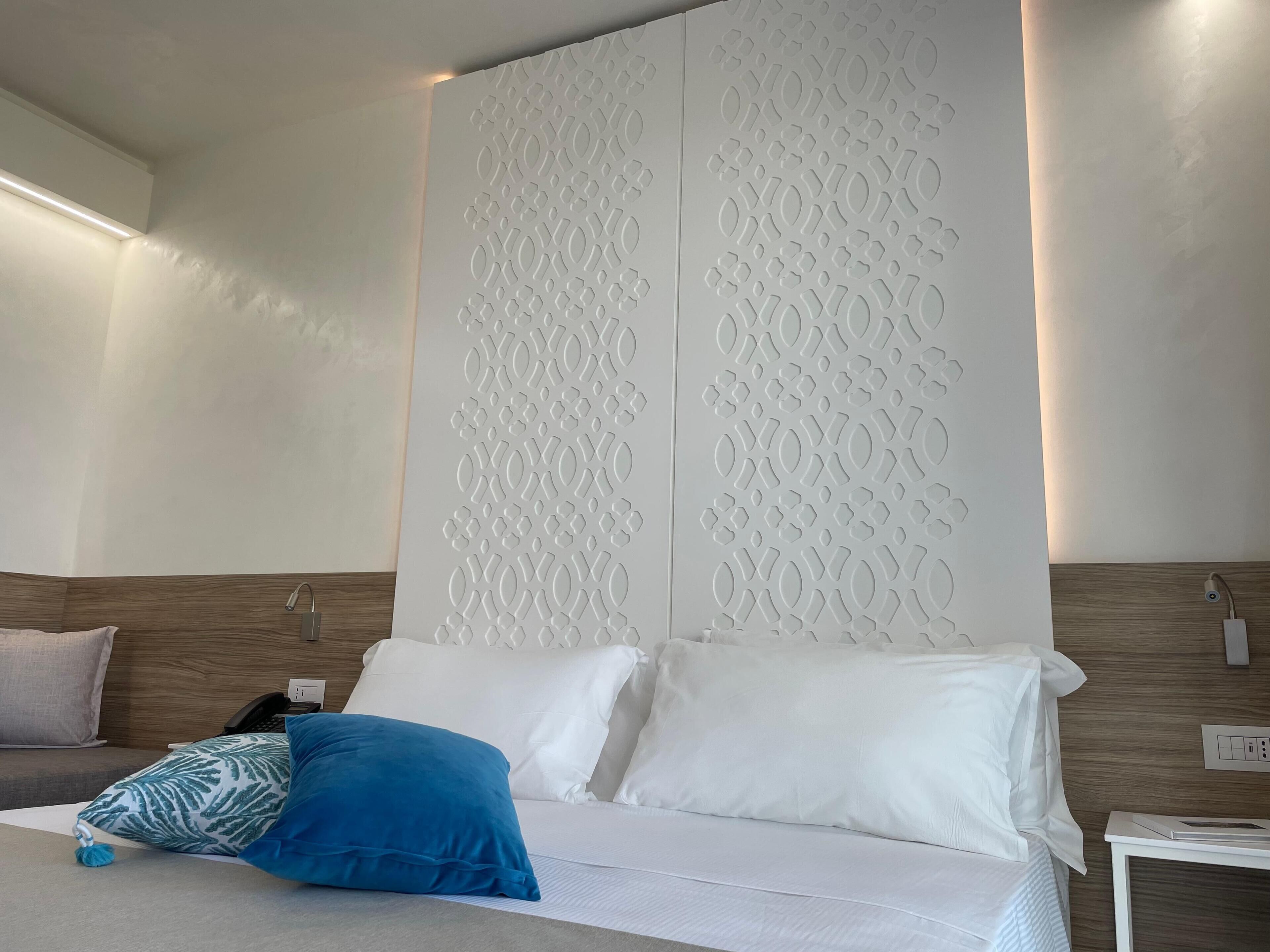 A modern hotel room with a large bed, white bedding, and a decorative wall panel.