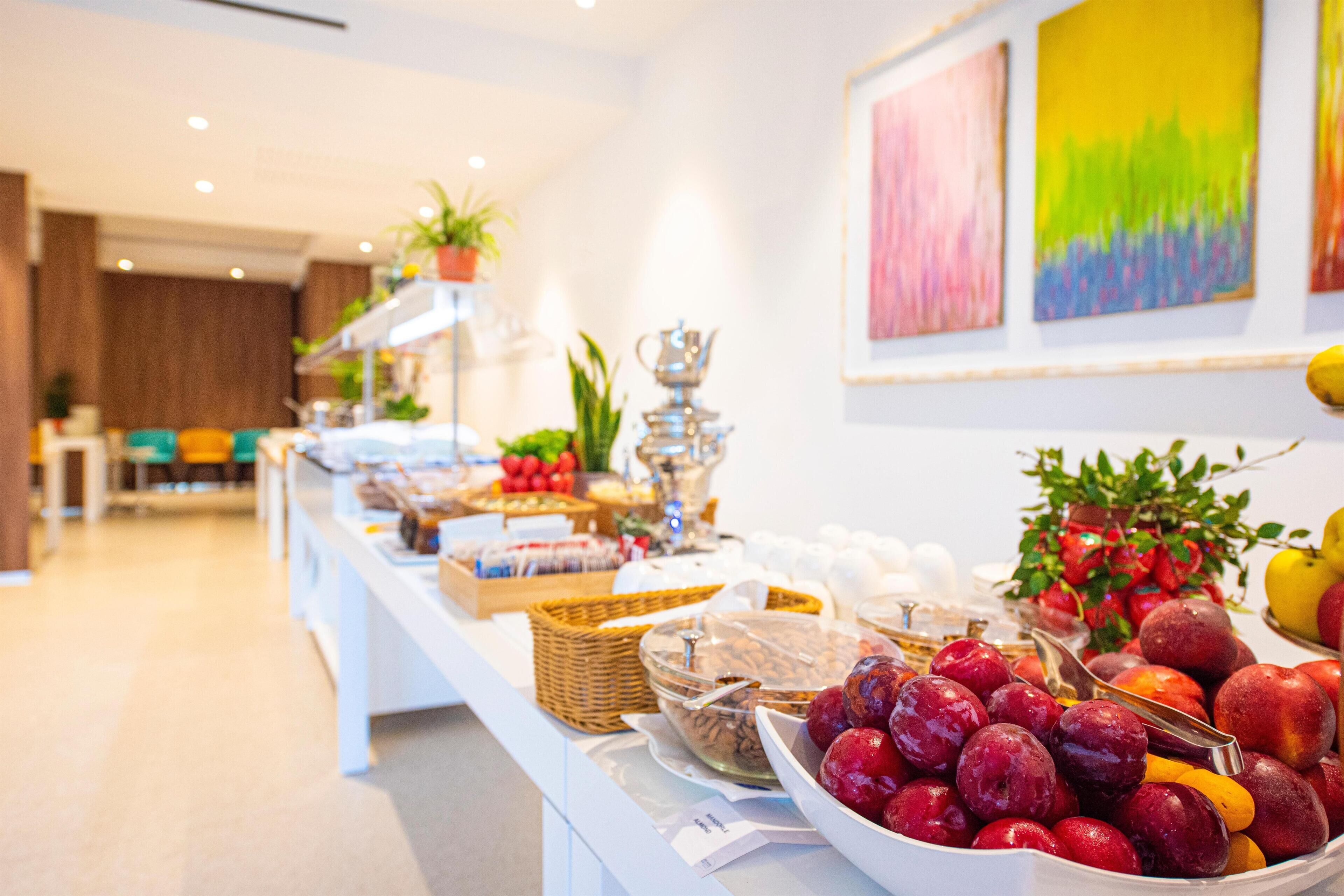 A buffet table with various fruits and dishes, a plant on a shelf, and a painting on the wall.