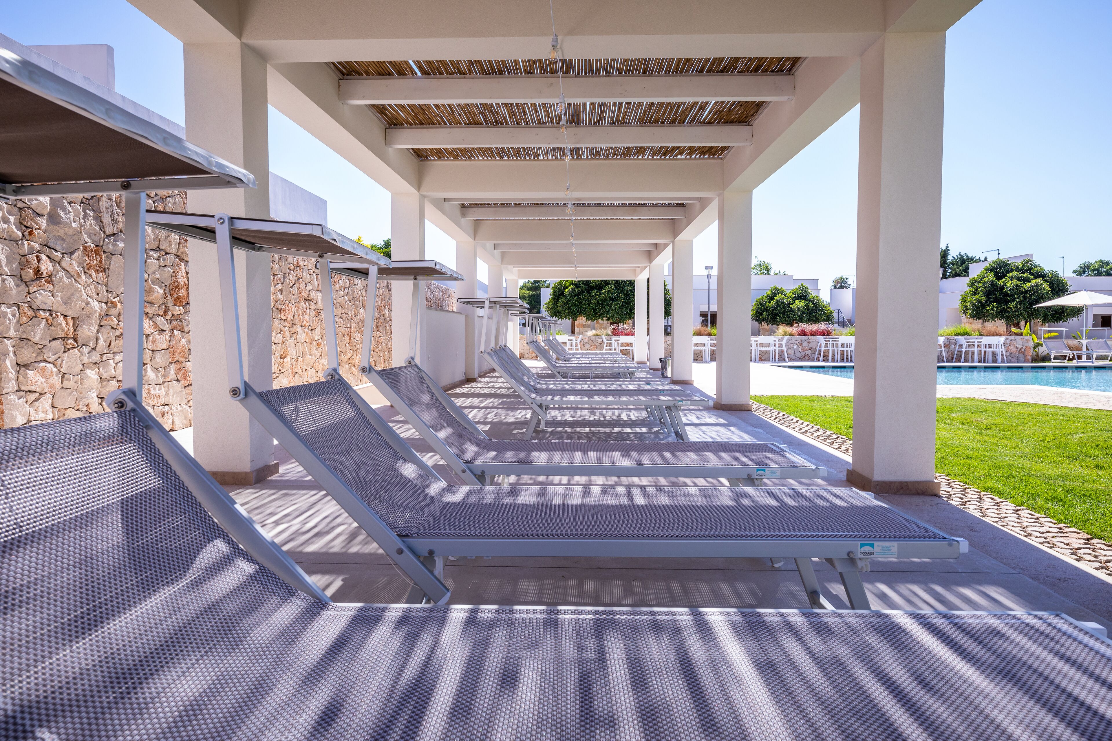 A covered outdoor seating area with metal loungers and a stone wall backdrop.