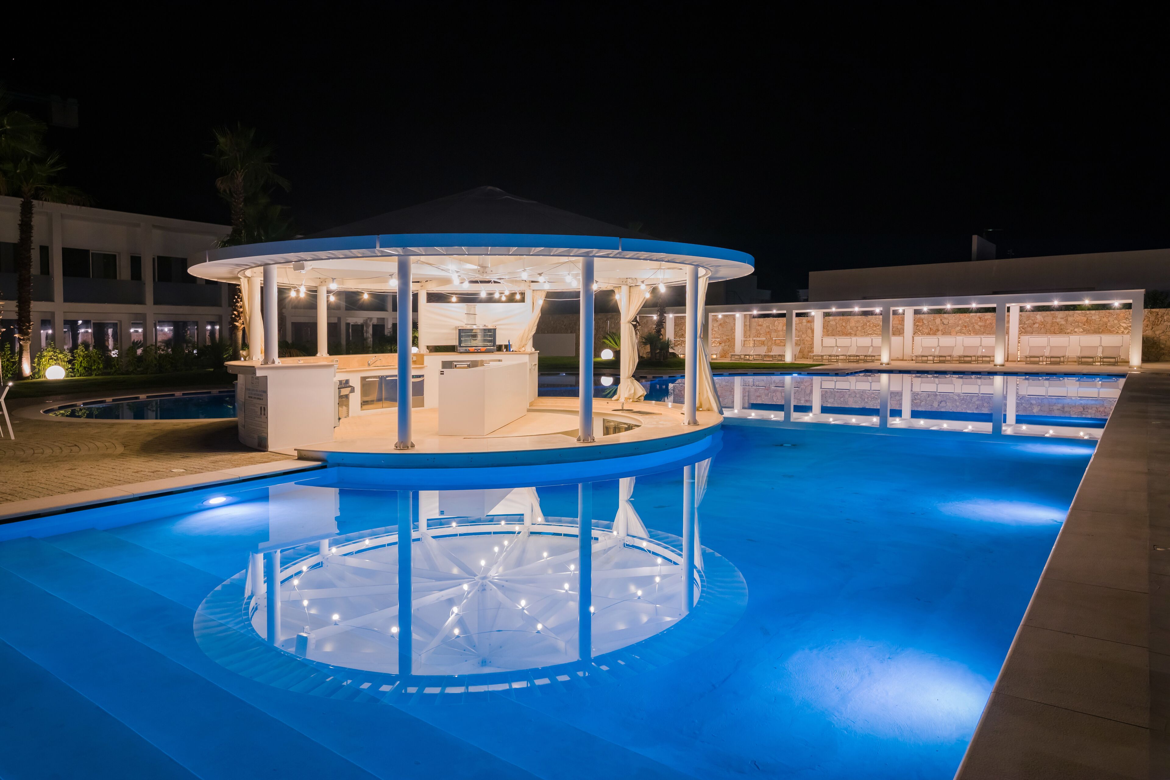 A circular pool with a central bar area and seating around it, surrounded by a covered pavilion.
