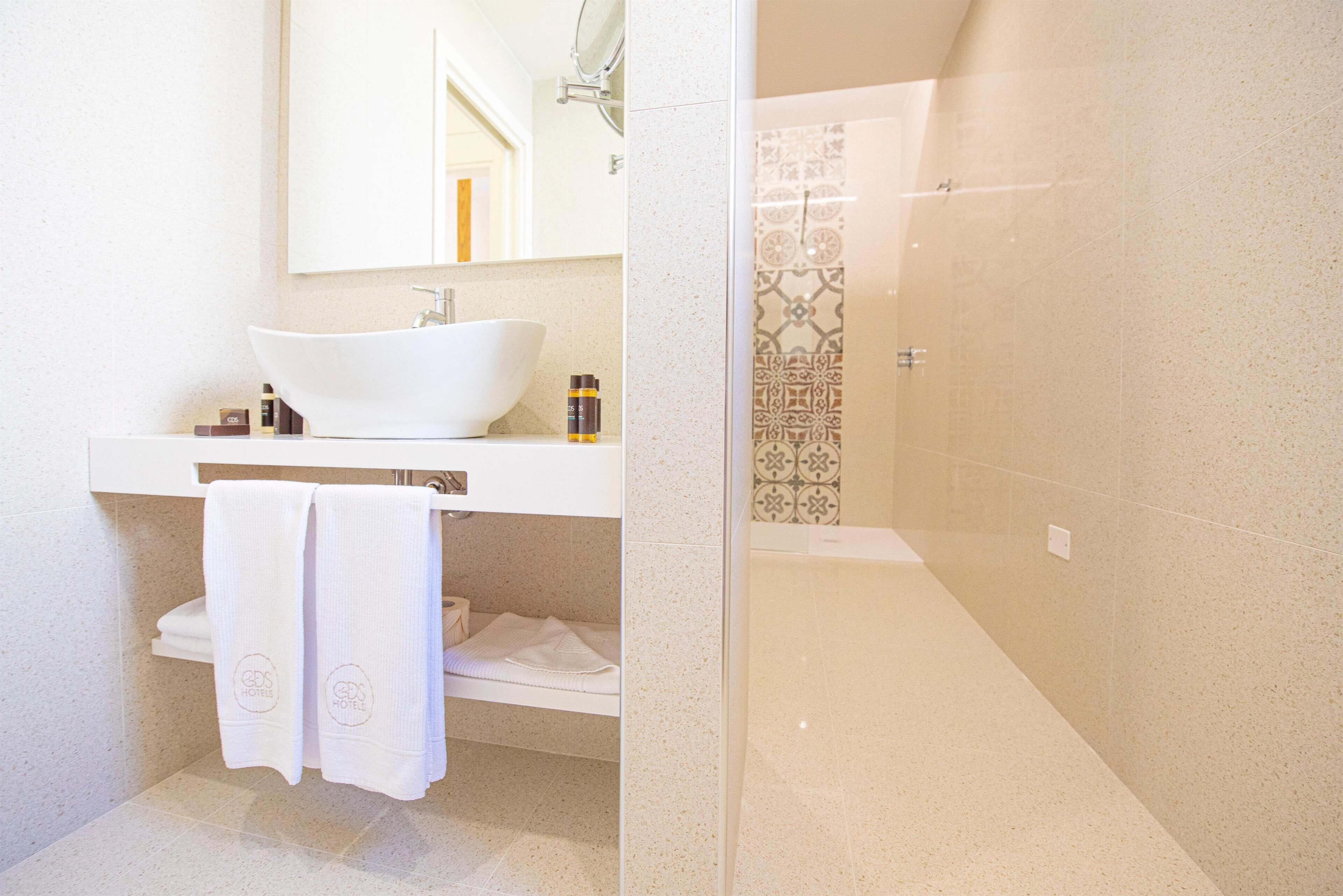 Un baño con lavamanos blanco, espejo, toallero y zona de ducha.
