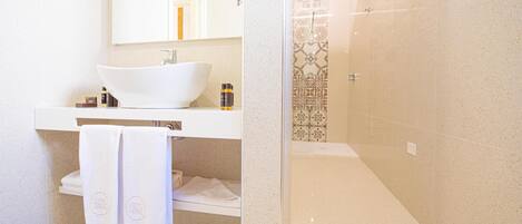 Un baño con lavamanos blanco, espejo, toallero y zona de ducha.