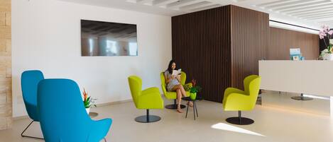 Un área de recepción moderna con sillas amarillo brillante, un mostrador de recepción blanco y un cuadro abstracto grande en la pared.