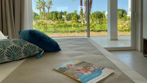Un dormitorio con un ventanal grande, una cama con almohadones estampados y un libro en el suelo.