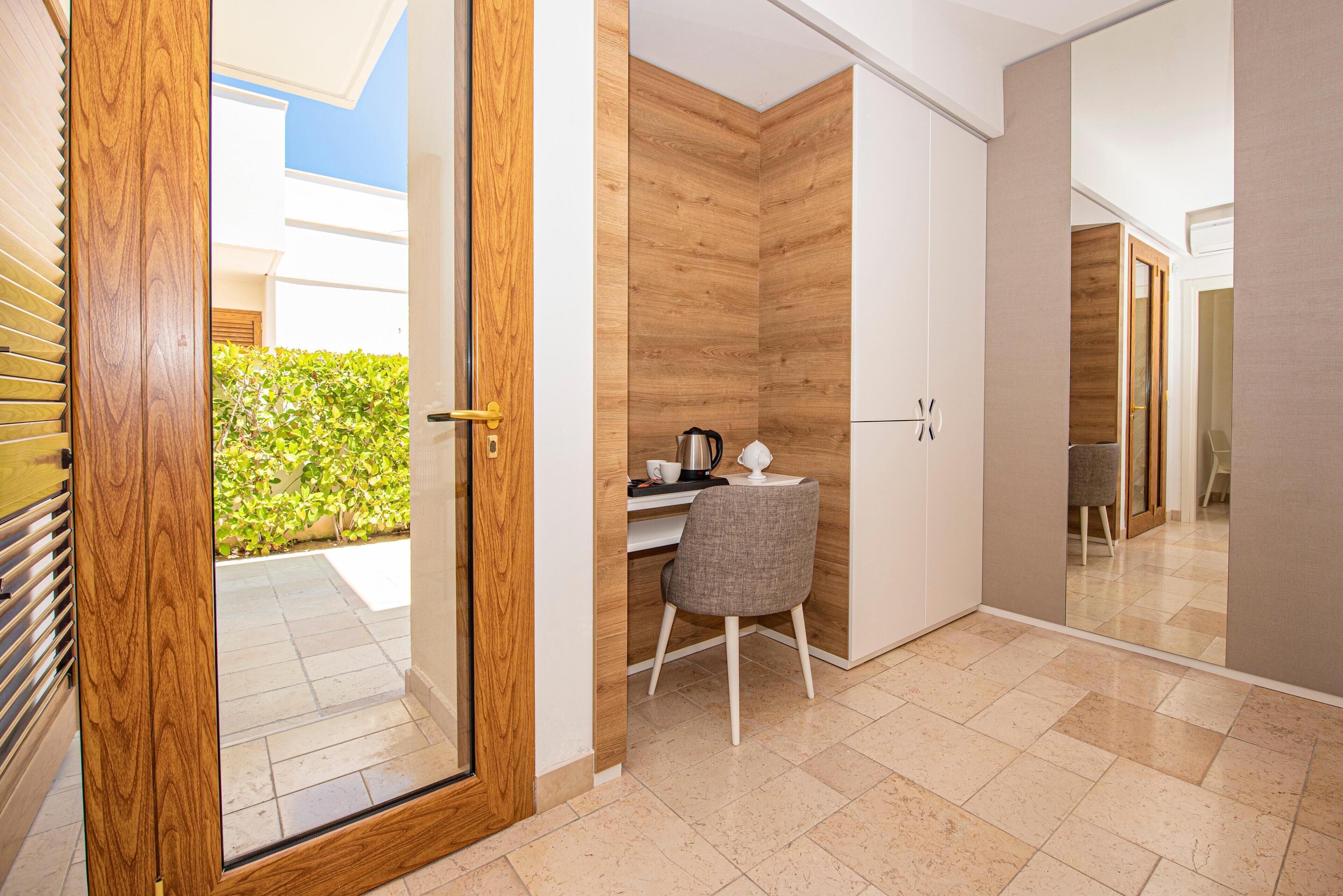 A modern room with a wooden door, a desk with a chair, and a view of a garden outside.