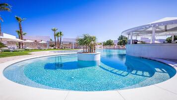 A circular pool with a central island, surrounded by lounge chairs and palm trees.