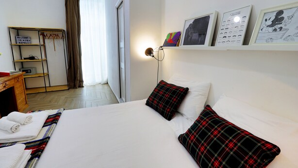 A hotel room with a bed, pillows, a bedside table, a lamp, a wardrobe, and a sign. - Palazzo Bevilacqua Napoli B&B (Naples)