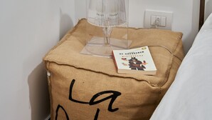 A small bedside table with a clear lamp, a book, and a pillow with text. - Palazzo Bevilacqua Napoli B&B (Naples)