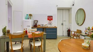 A compact kitchen with a dining area, featuring a wooden table, chairs, and a small island with a sink. - Palazzo Bevilacqua Napoli B&B (Naples)
