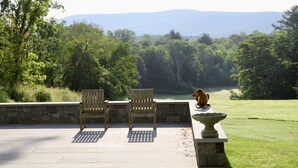 A patio with two wooden chairs and a stone table, overlooking a grassy area with trees and a distant mountain range. - Inn at Kenmore Hall (Richmond)
