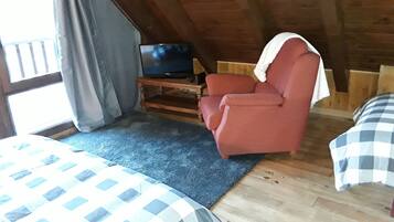 A cozy room with a bed, a red armchair, a television on a wooden stand, and a window with curtains.