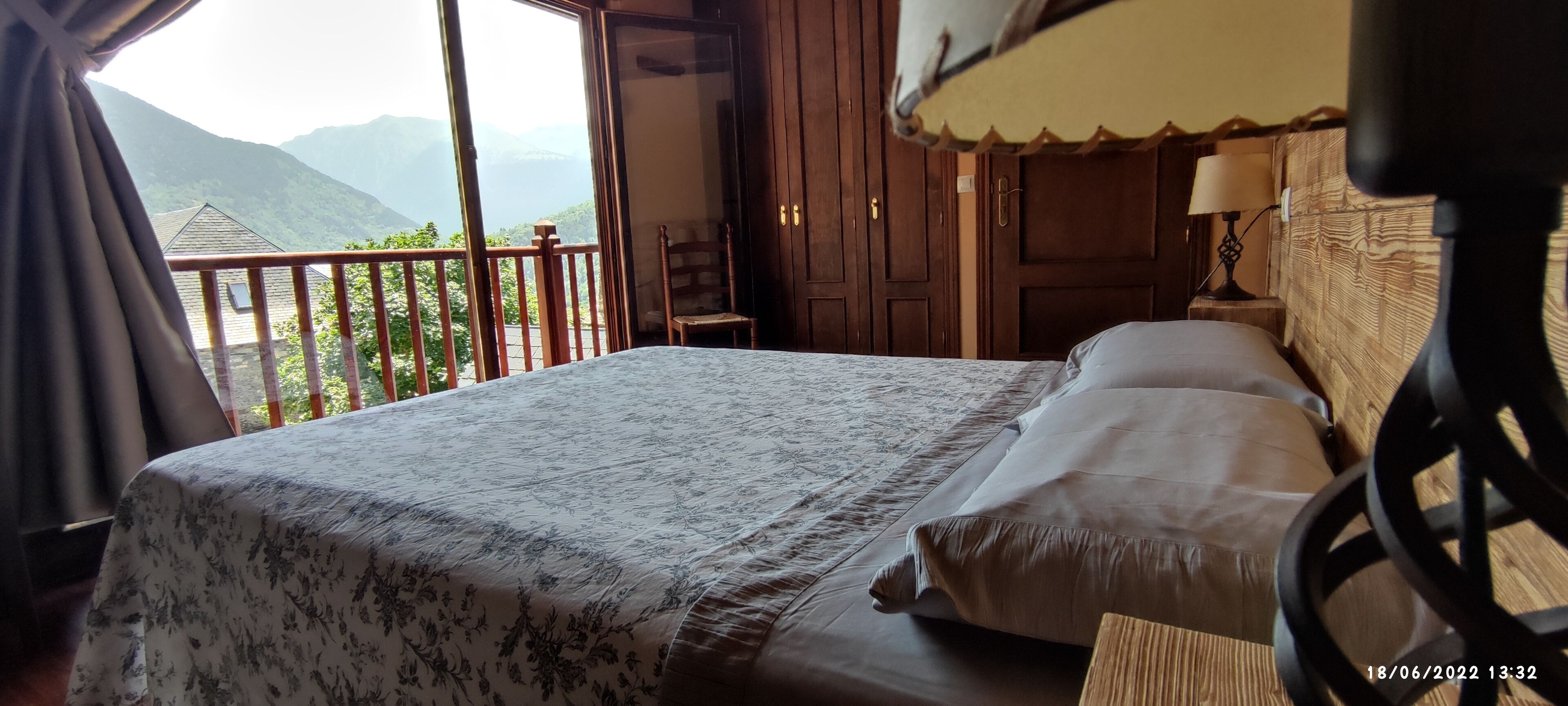 Een slaapkamer met een groot bed, houten hoofdbord en uitzicht op bergen vanuit een balkon.