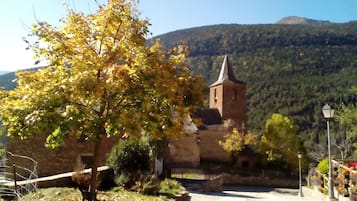 Un bâtiment historique en pierre, doté d’une tour, entouré d’un mur de pierre et d’un arbre aux feuilles jaunes.