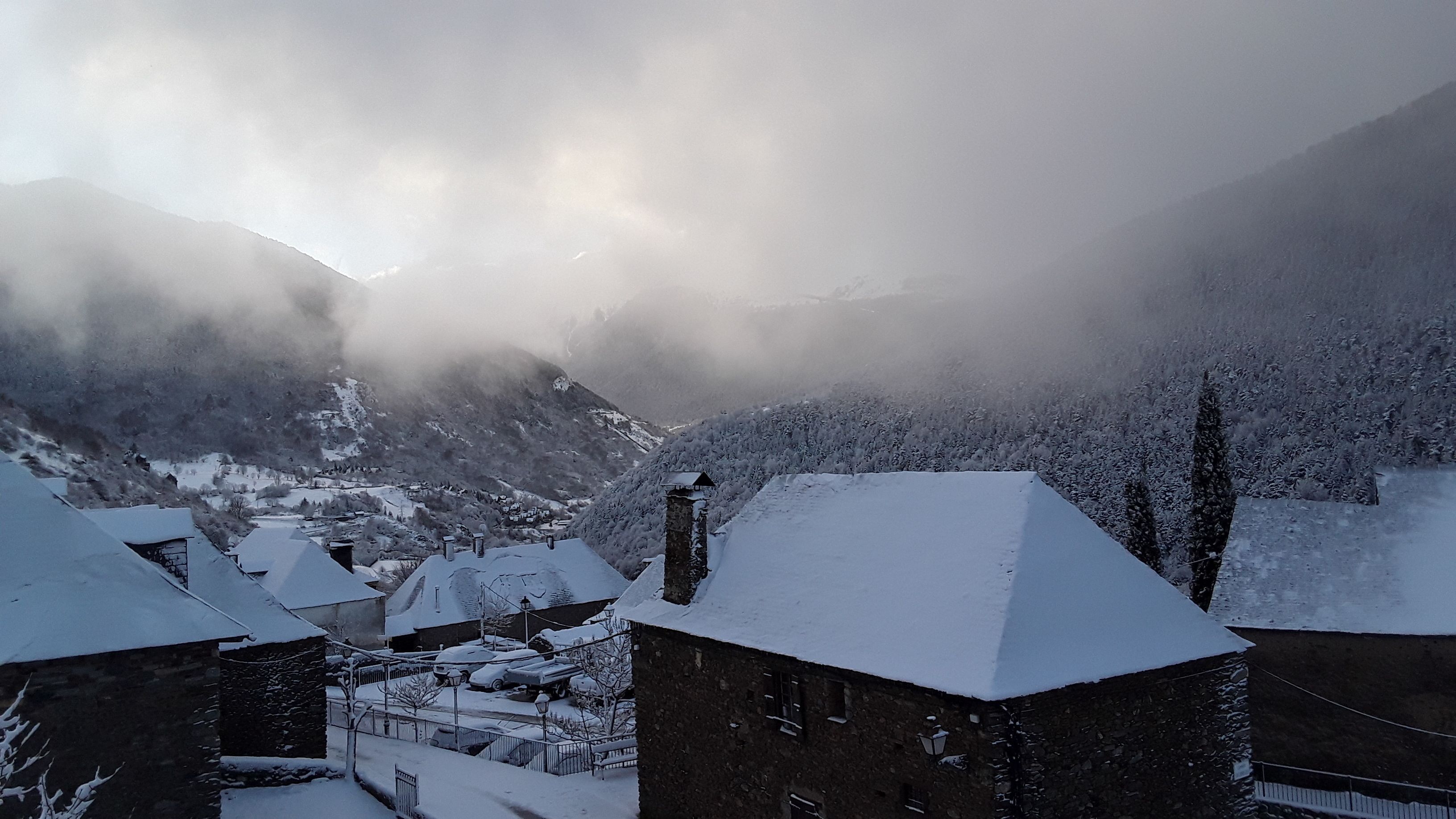 A snow-covered village with traditional stone buildings, a church, and a mountain backdrop.