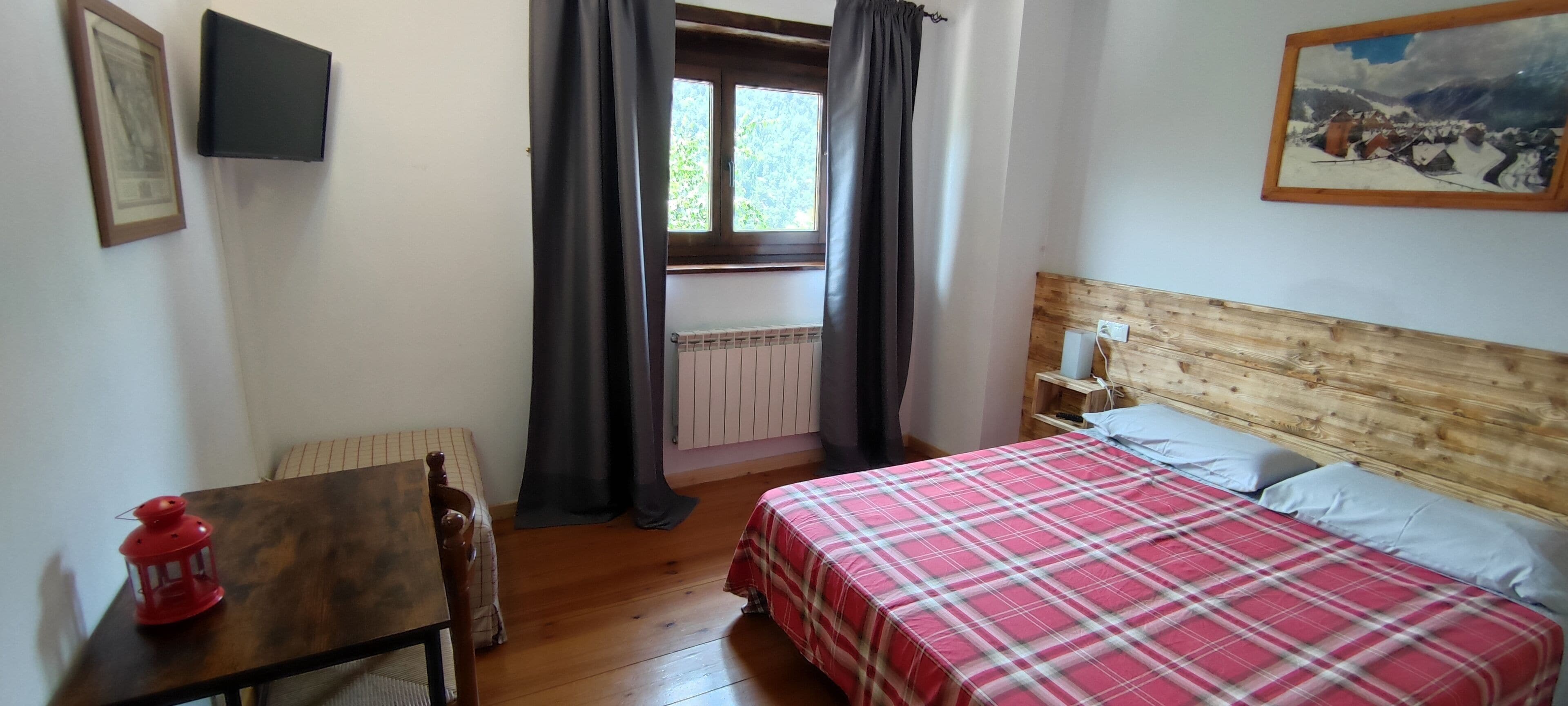 A bedroom with a bed, a wooden headboard, a nightstand, a red lantern, a window with curtains, and a painting on the wall.
