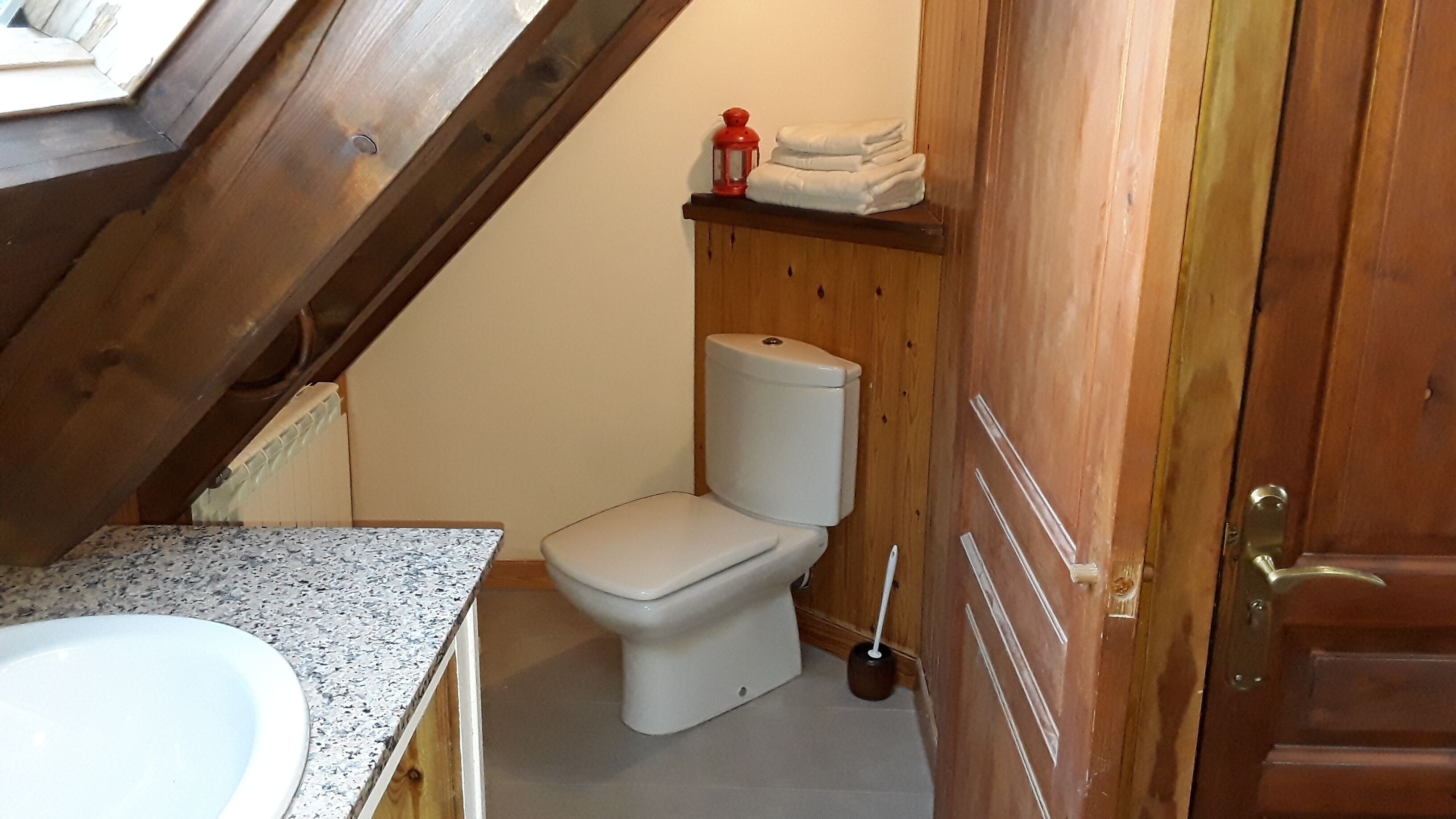 A small bathroom with a toilet, a sink, and a wooden shelf with towels.
