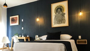 A modern hotel room with a large bed, bedside tables, a desk, and a chair. There are framed artworks on the walls and pendant lights above the bed. - Romance City Hotel (Morelia)