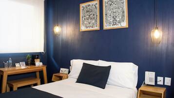 A hotel room with a bed, bedside tables, a desk, and artwork on the wall.