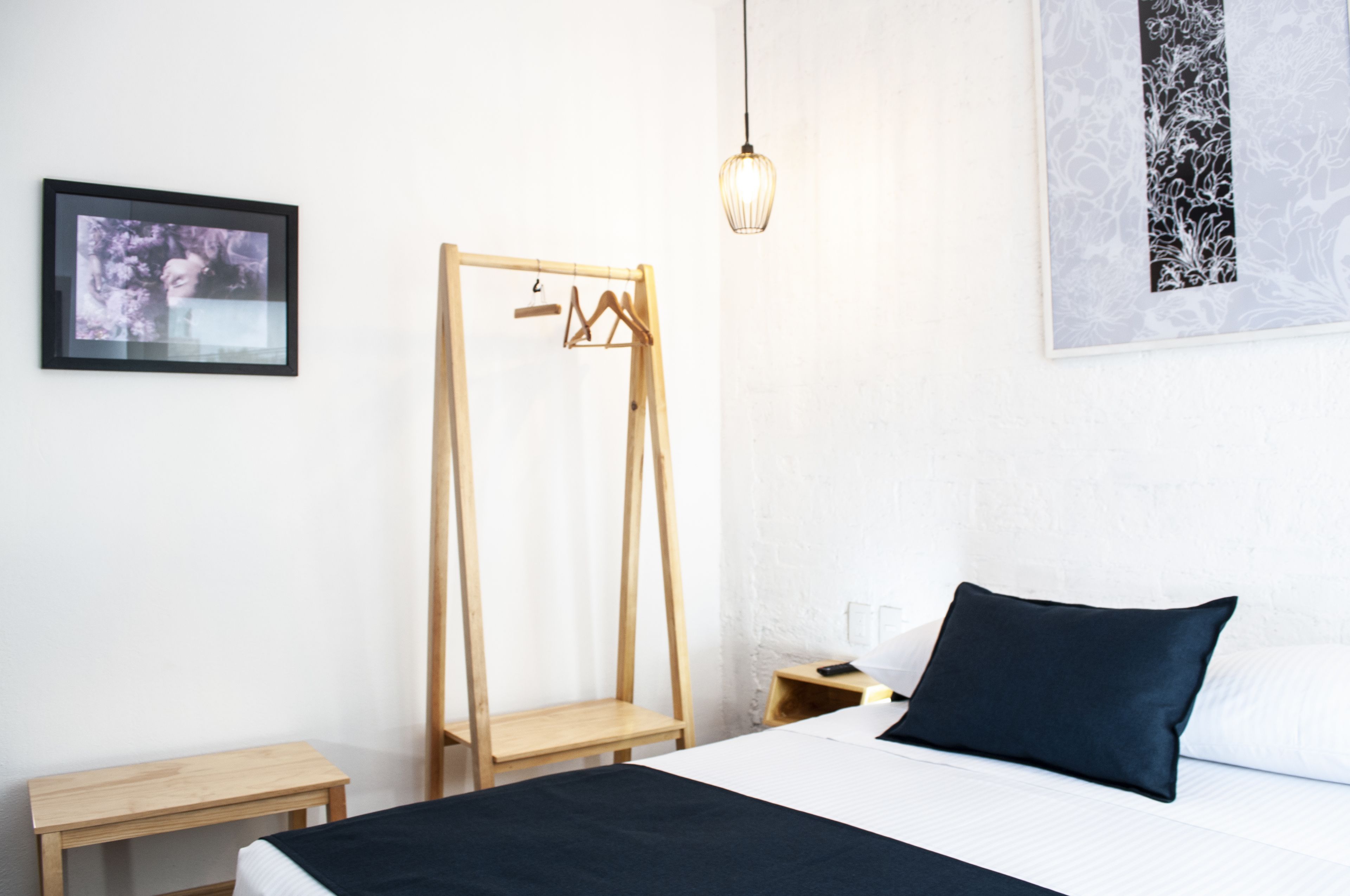 A bedroom with a bed, a wooden wardrobe, a small table, a hanging light fixture, and a framed picture on the wall.