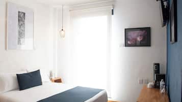 Une chambre d’hôtel avec un lit, une table de chevet avec une machine à café, un tableau au mur et une fenêtre avec un rideau.