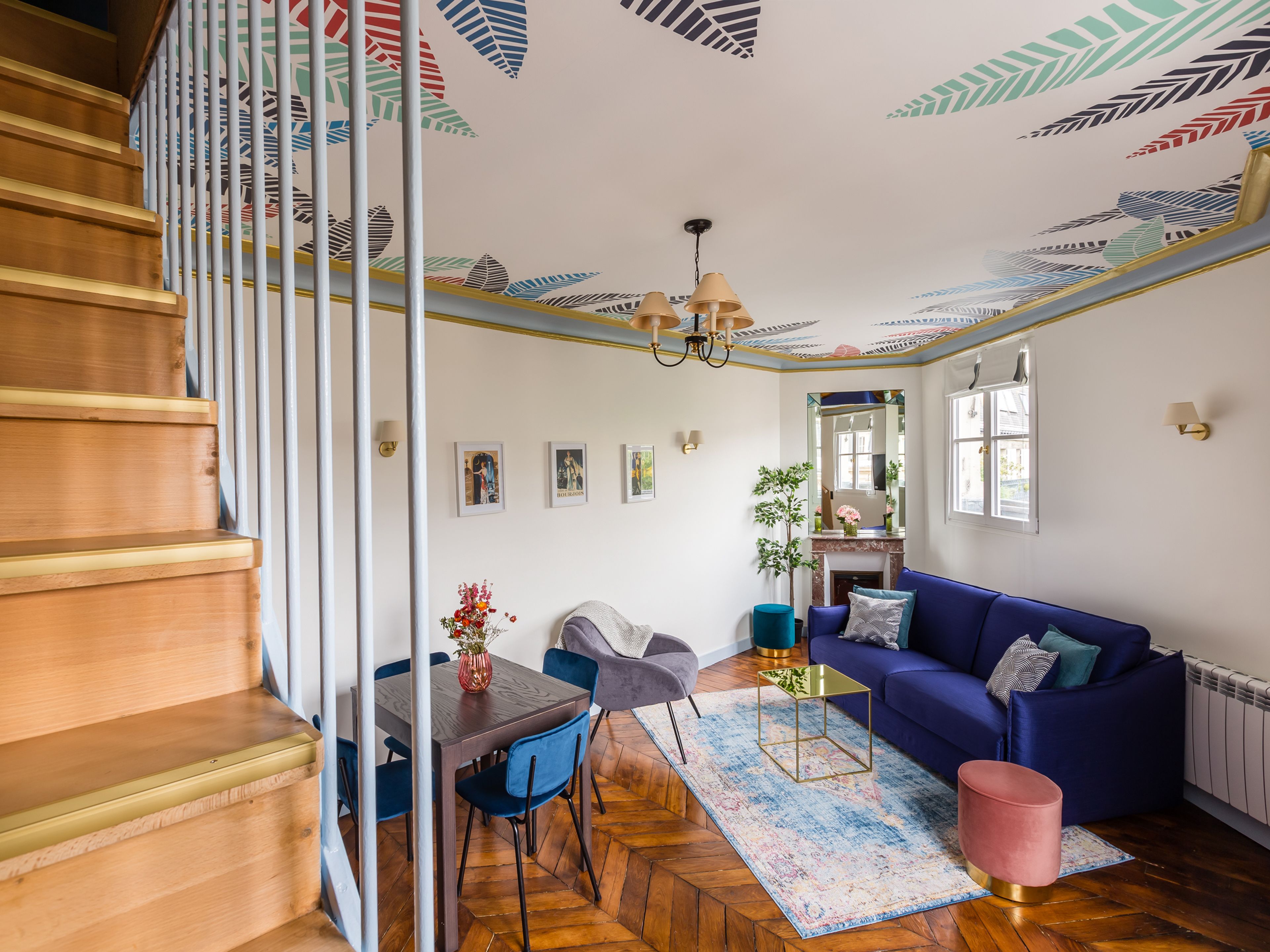 A spacious living room with a blue sofa, a wooden staircase, and a herringbone-patterned floor.