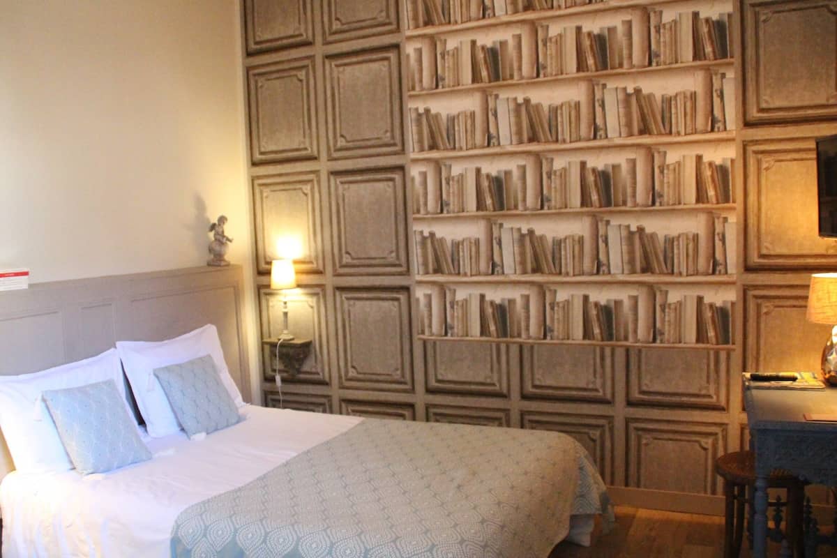 Une chambre d’hôtel avec un grand lit, une bibliothèque, un bureau et une chaise.