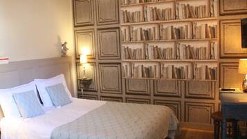 A hotel room with a large bed, a bookshelf, a desk, and a chair.