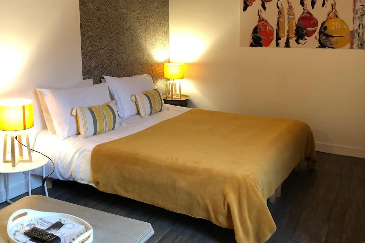 Une chambre d’hôtel avec un lit, deux lampes de chevet, une table avec une télécommande, un mur à motifs et un tableau.