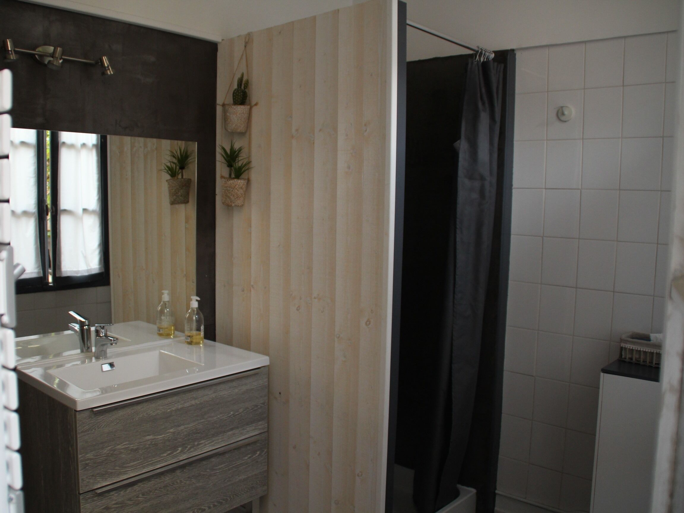 A bathroom with a double sink, a mirror, a shower curtain, and two potted plants.