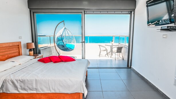 Une chambre d’hôtel avec un lit, un fauteuil suspendu, une télévision et un balcon donnant sur la mer.