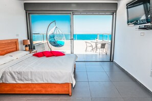 Habitación de hotel con cama, una silla colgante, televisión y balcón con vista al mar.