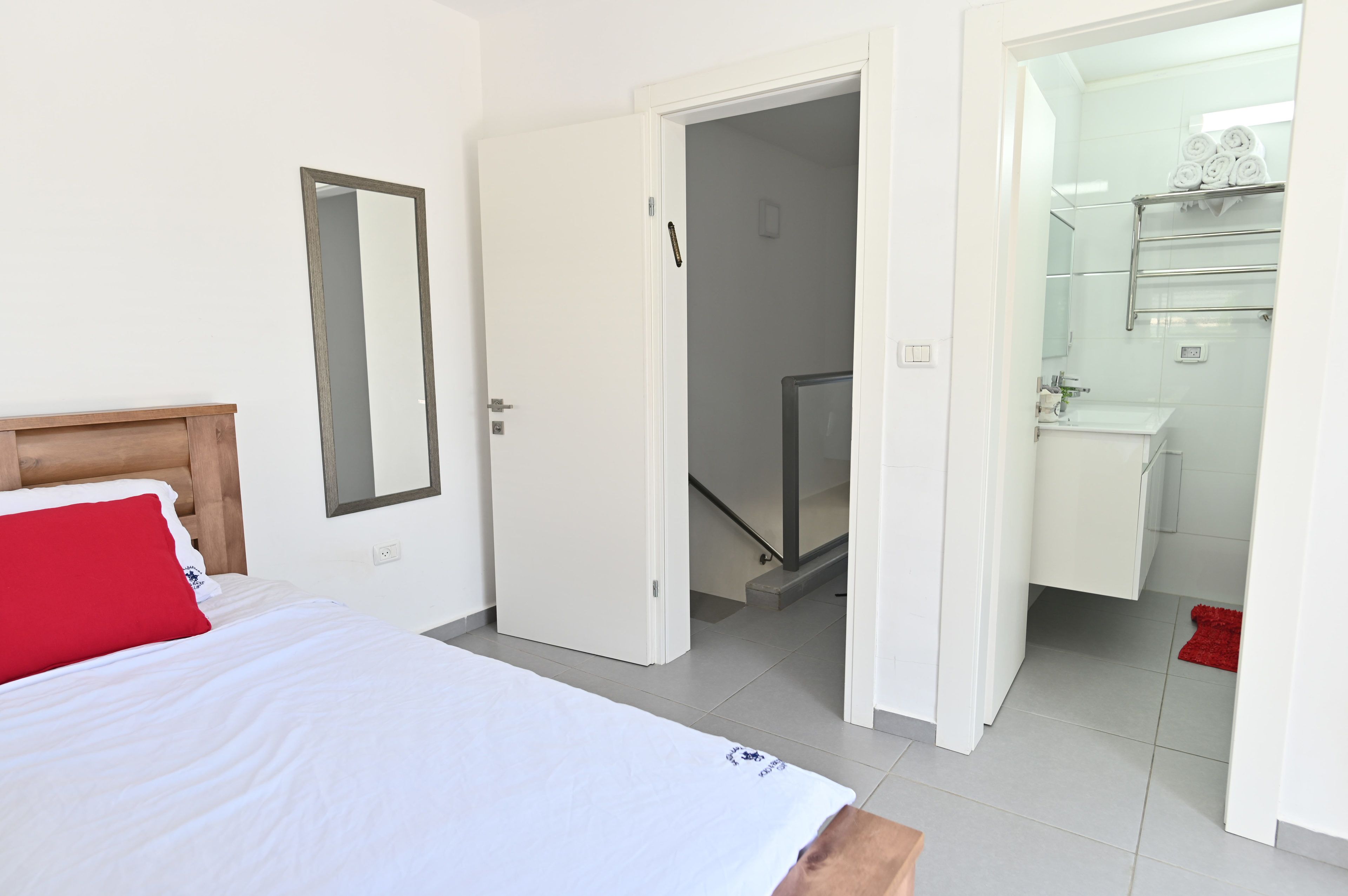 A bedroom with a bed, a mirror, and a bathroom with a shower and a towel rack.