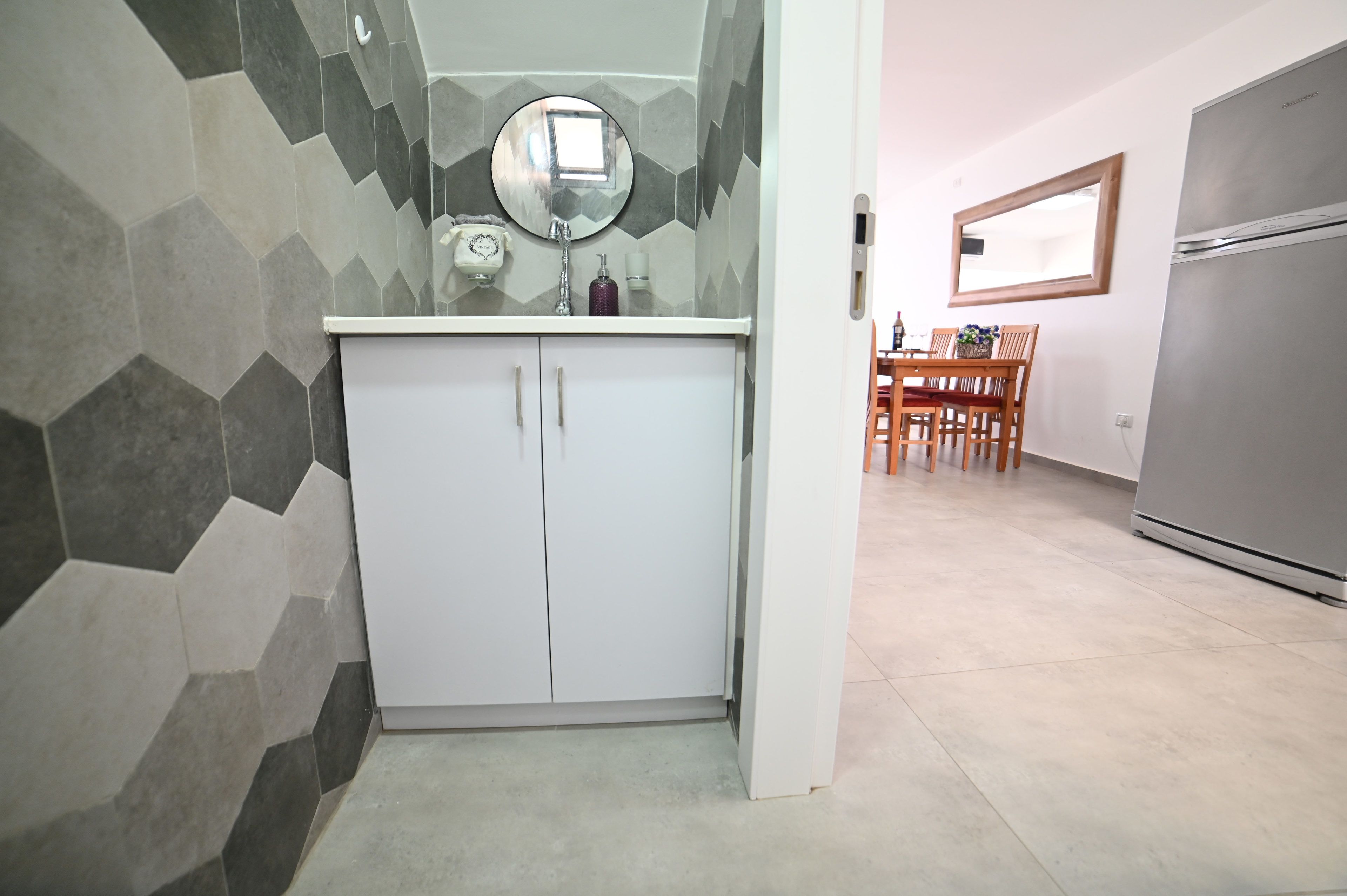 A modern kitchen with a white cabinet, a round mirror, and a hexagonal tile backsplash.