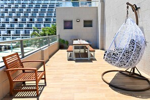 Un balcón con banca de madera, una silla colgante y una mesa con sillas.