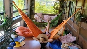 Una habitación con una hamaca, un sofá y una mesa con un libro y un sombrero.
