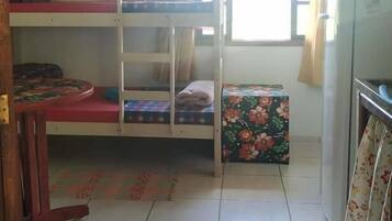 A dormitory room with bunk beds, a small table, a refrigerator, and a window with curtains.