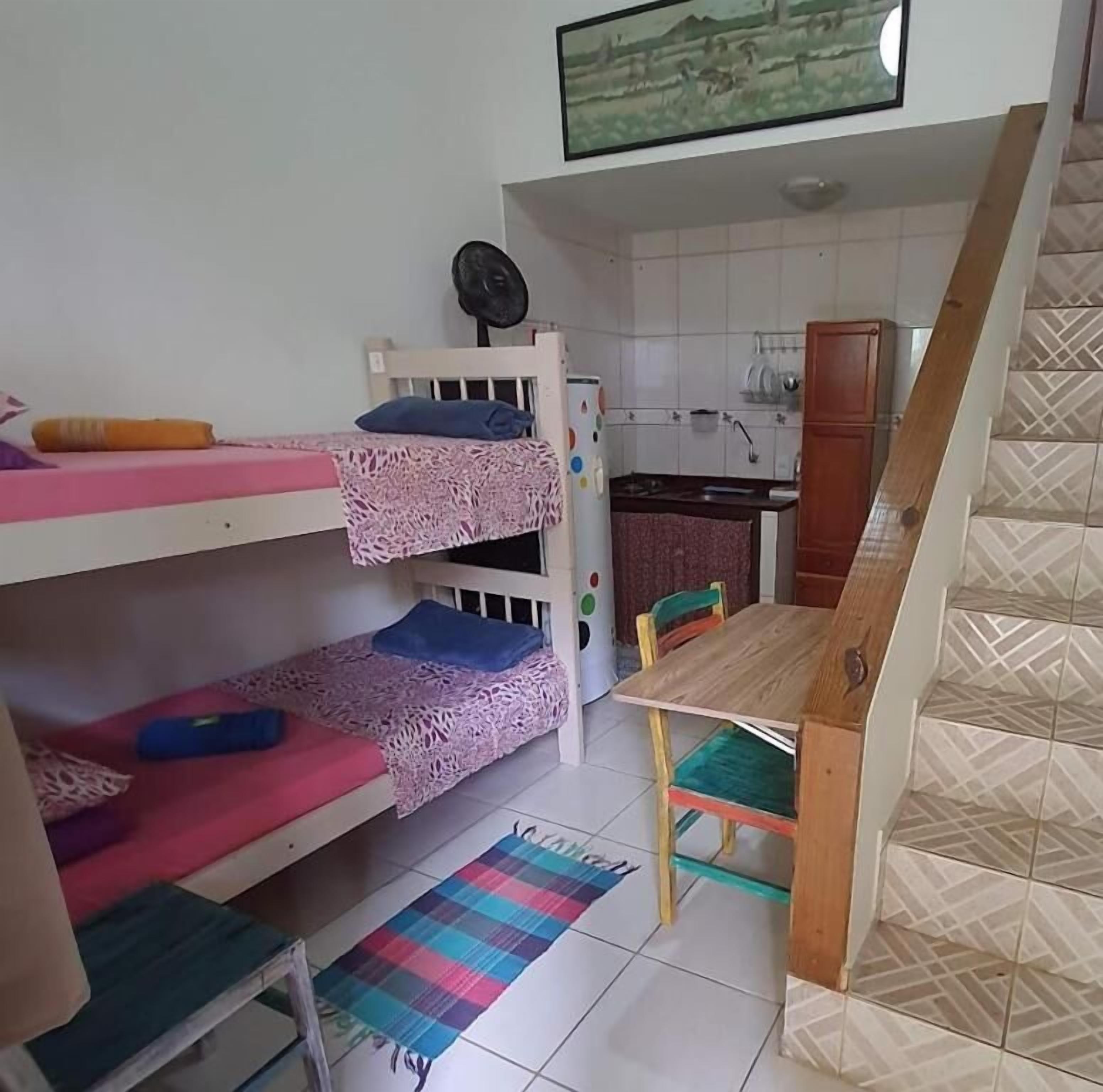 A dormitory room with bunk beds, a small kitchen area, and a wooden table with chairs.