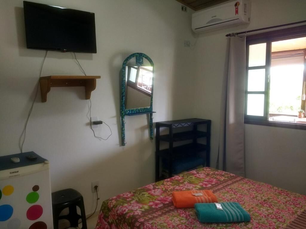 A bedroom with a bed, a TV mounted on the wall, a mirror, and a small desk with a computer.
