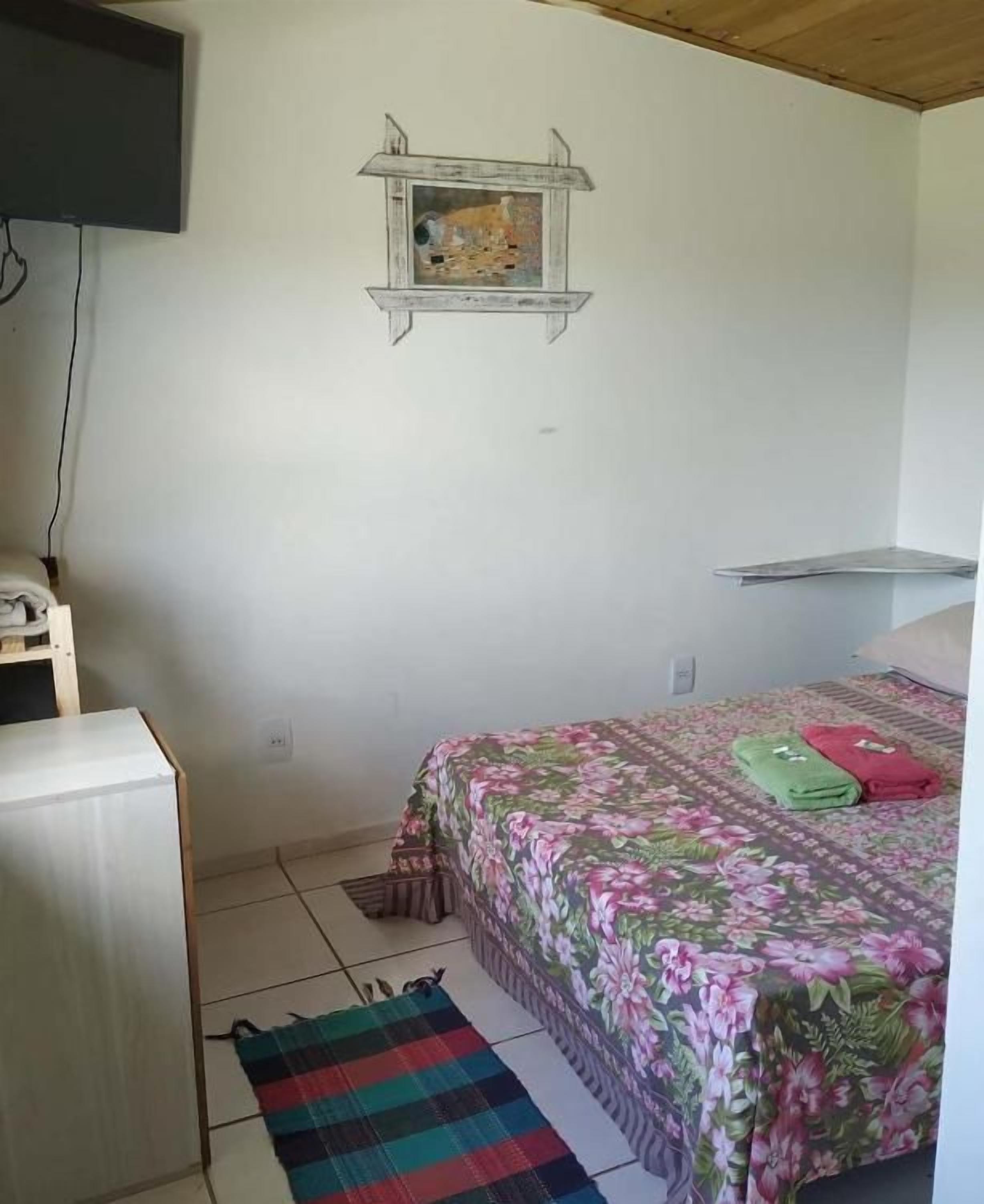 A bedroom with a bed, a small desk, a TV mounted on the wall, and a shelf.