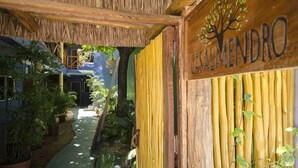 A wooden sign with a tree logo and the name "CASALMENDRO" in a courtyard with potted plants and a thatched roof. - Casa Almendro (Tulum)