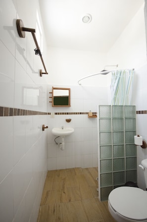A bathroom with white tiles, a wooden floor, a sink, a toilet, a shower with a glass door, and a towel rack.