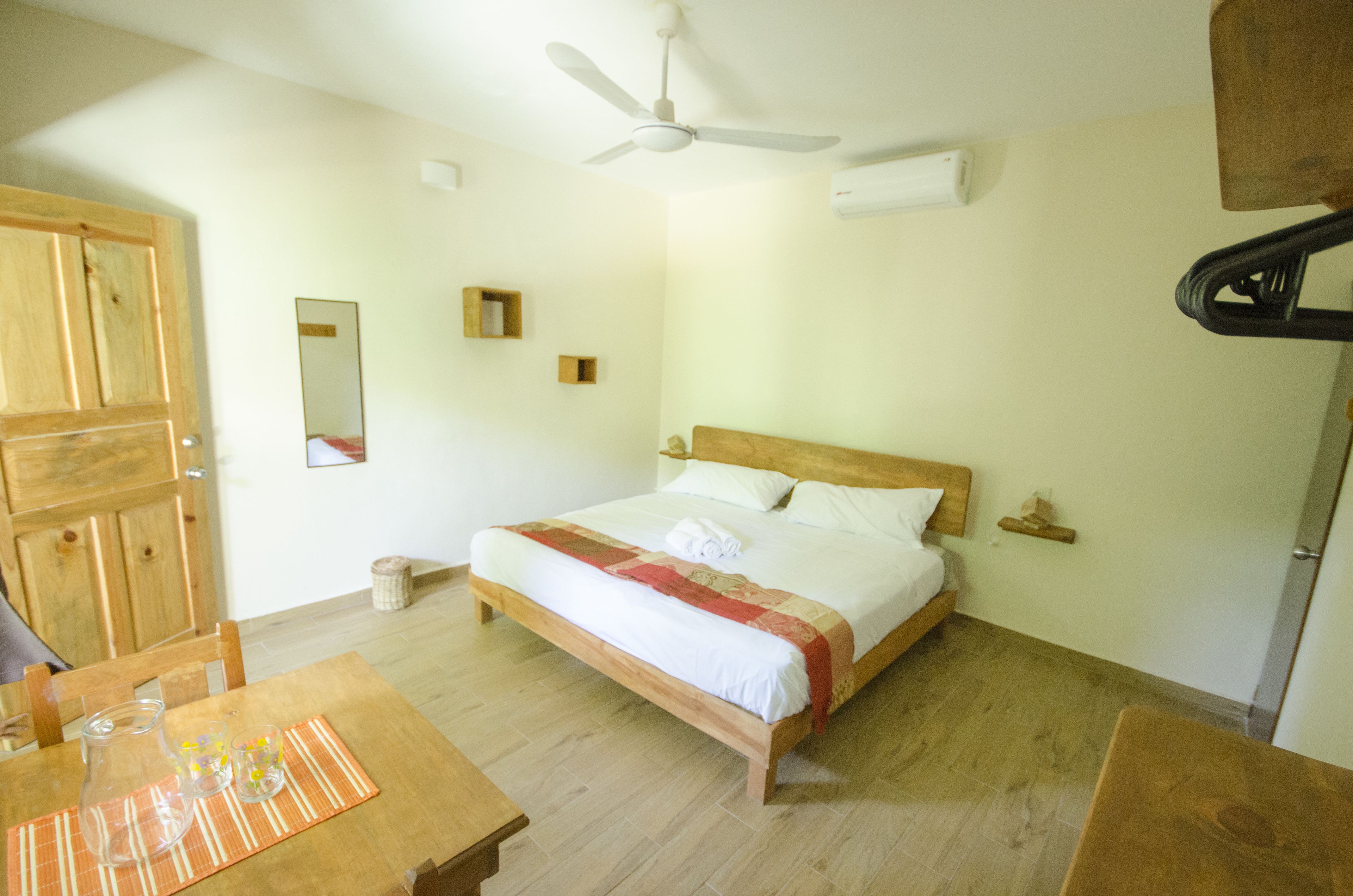 Ein Schlafzimmer mit einem hölzernen Bett, einem Deckenventilator, einem Holztisch mit Unterlage und einem Holzkasten.