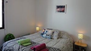 A bedroom with a patterned bedspread, two bedside lamps, a wall-mounted air conditioner, a small potted plant, and a framed artwork on the wall. - Beautiful Quiet Apartment Near Aristides (Mendoza)