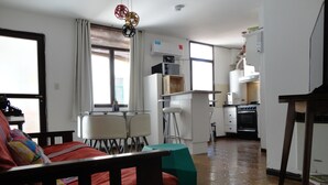 A living room with a sofa, a dining table with chairs, a kitchen area with a stove and refrigerator, and a window with curtains. - Beautiful Quiet Apartment Near Aristides (Mendoza)